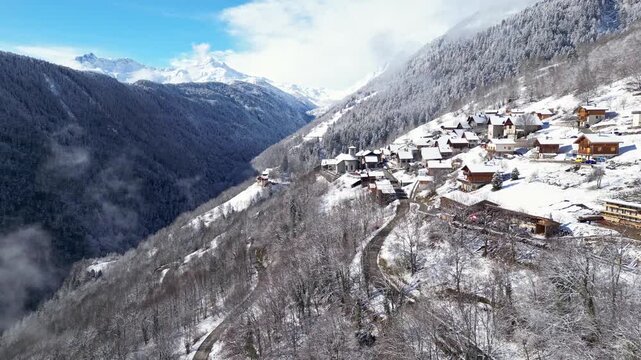 Aerial view of a snowy alpine village with chalets in Tarentaise Valley surrounded by forest and mountains in the French Alps, Savoie, France.