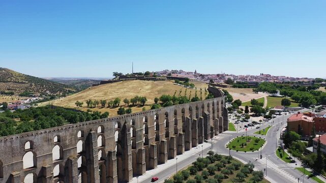 Aerial view of the historic Amoreira Aqueduct in Elvas, Portugal, with surrounding cityscape and countryside under a clear blue sky.