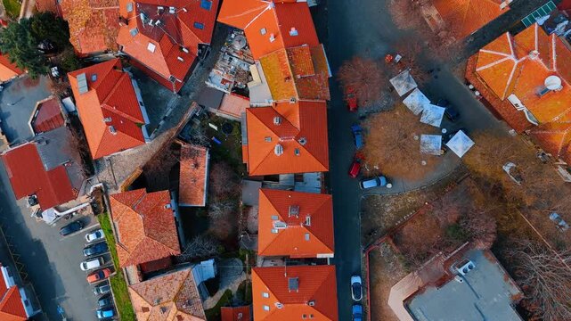 Nadir aerial shot of narrow street and red roofs. City rooftops and cobblestone street with parked cars.