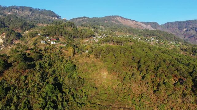 Scenic aerial shot of lush green mountains and scattered rural homes in Bontoc, Philippines, under clear blue sky.