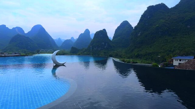 Guilin Yangshuo China, luxury infinity pool with crescent moon decor, karst mountains, tranquil resort vibe.luxury infinity pool at a mountain resort, showing a white crescent moon sculpture 