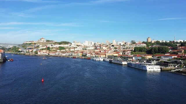 Scenic view of Porto city with colorful buildings along the Douro River and the iconic Dom Luis I Bridge under a clear blue sky.
