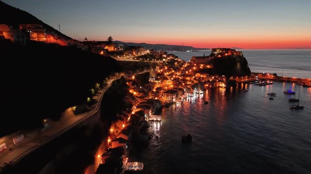 Night aerial view of Chianalea Scilla with glowing village lights and coastline