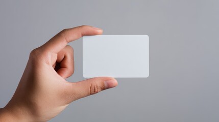 Fototapeta premium Elegent photo of hand holding blank white plastic credit card presenting a mock-up template on a plain studio background with copy space for banking or identity design concept.