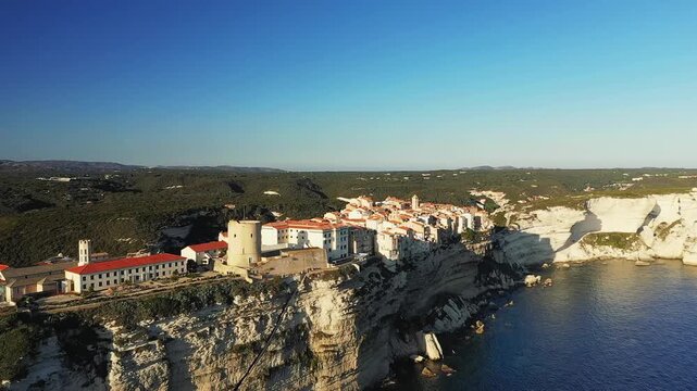 Aerial view of Bonifacio s historic buildings perched dramatically on white limestone cliffs above the Mediterranean Sea in Corsica, France, under a clear blue sky.