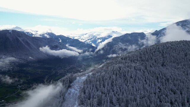Aerial view of snowy Tarentaise Valley in the French Alps with fog, pine forests and dramatic winter mountains in Savoie, France.