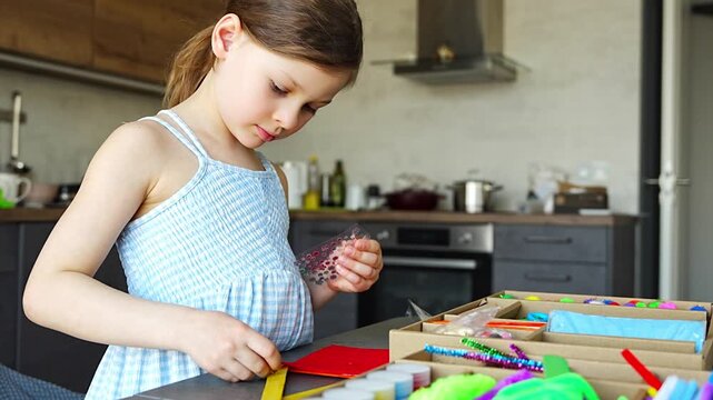 Little girl decorating handmade craft with colorful self adhesive rhinestones at table. Kids creativity fine motor skills development and learning through play concept.