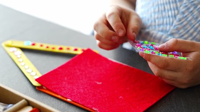 Close up view of hands of little girl decorating handmade craft with colorful self adhesive rhinestones at table. Kids creativity fine motor skills development and learning through play concept.