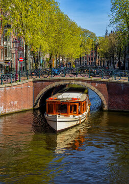 Tourist canal boat passing under a bridge, Jordaan neighbourhood, Amsterdam, Netherlands &mdash; canal cruise