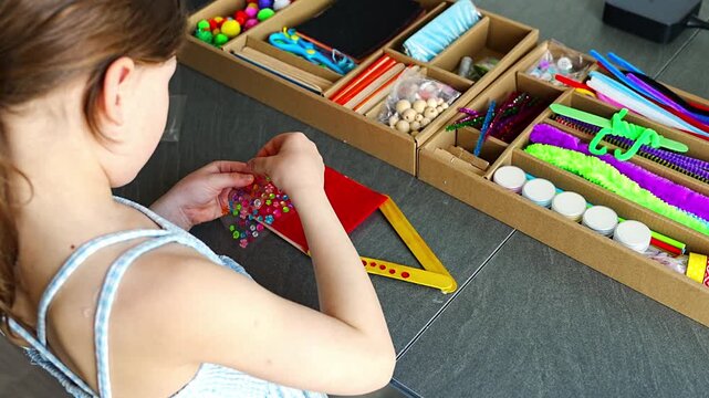 Little girl decorating handmade craft with colorful self adhesive rhinestones at table. Kids creativity fine motor skills development and learning through play concept.