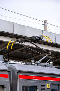 Close-up of a commuter train pantograph mounted on a carriage roof, collecting electric current from overhead lines in an electrified railway system.