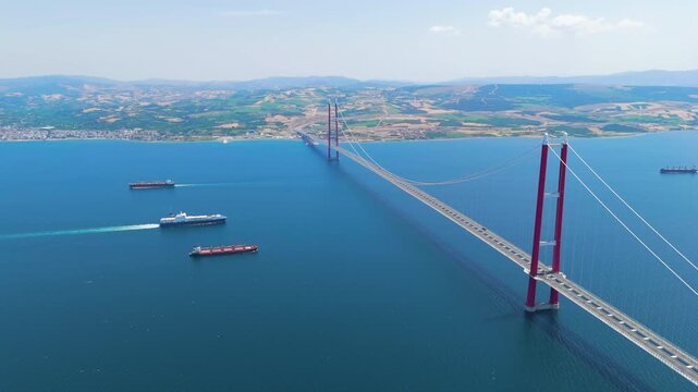 Lapseki, Turkey. 1915 Canakkale Bridge with moving cars above and multiple cargo ships and a passenger ferry on the Dardanelles below. Aerial View