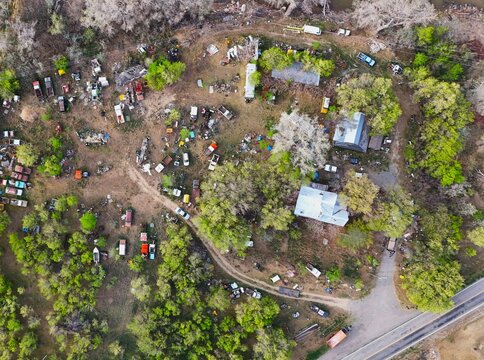 Aerial view of a sprawling junkyard with colorful car bodies scattered amidst trees and buildings, creating a vibrant yet chaotic landscape, Palisade, Colorado, USA.