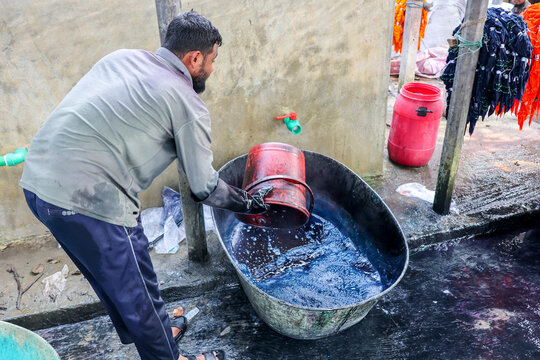 Narayanganj, Bangladesh - 29 March 2026: View of a worker in gloves pouring water into a tub of indigo dye, creating a striking contrast against the weathered wall.