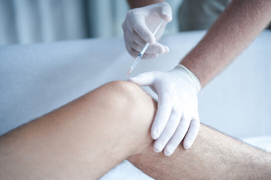Doctor giving injection into patient knee. Close-up of medical procedure for pain relief, orthopedic treatment and therapy concept, healthcare professional wearing gloves.