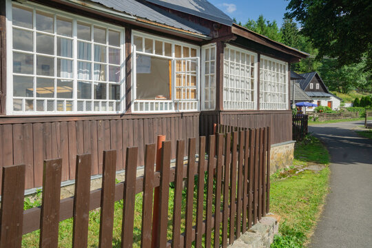 View of rustic charm with a dark wooden house featuring bright white-framed windows and a quaint brown fence along a paved path, Donovaly, Banskobystricky kraj, Slovakia.