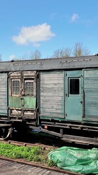 Dilapidated wooden railway carriages stand forgotten in a quiet shunting yard, their warped panels cracked and splintering with age.  Panning shot.