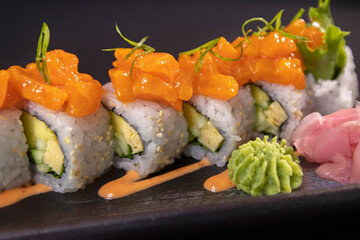 Delicious salmon sushi rolls with avocado and wasabi on black background. © Lan