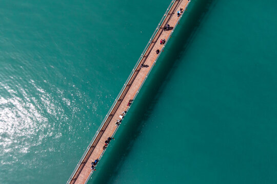 Aerial View of People Walking on Wooden Bridge Over Turquoise Water