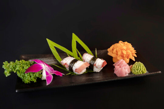 Premium octopus nigiri sushi (Tako) with nori seaweed wrap and artistic garnish on a black plate, dark background