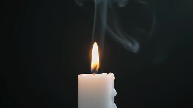 Close-up of a white candle burning with wisps of smoke rising against a dark background, creating