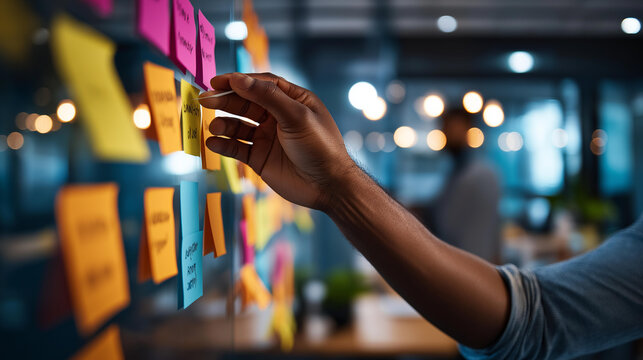 Close up of hands at a bright office kanban board with colored sticky notes arranged in development columns including backlog sprint review and done one hand moving a task