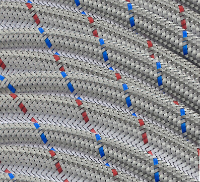 Coiled stainless steel hose with repetitive design woven pattern red, blue stripes. Industrial use, plumbing, maintenance projects. Braided industrial hose texture creating strong geometric background