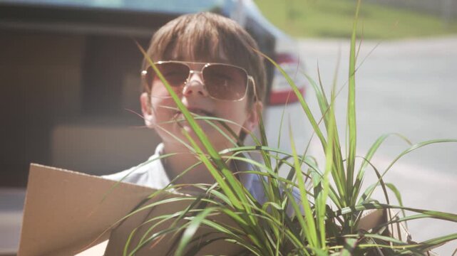 Young boy smiling with plant outside, Happy young child with sunglasses and plant during family move outside