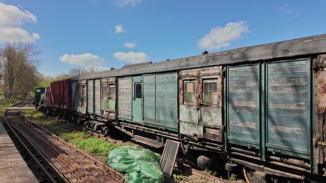 Dilapidated wooden railway carriages stand forgotten in a quiet shunting yard, their warped panels cracked and splintering with age.  Panning shot.