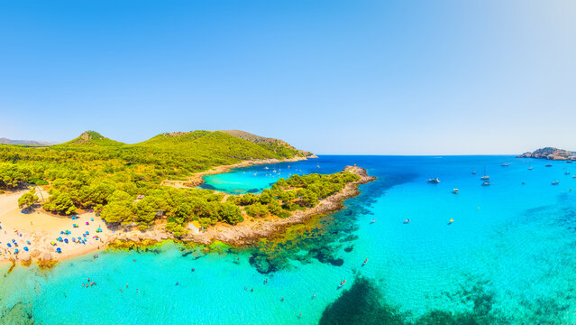 Aerial view of Cala Agulla beach and turquoise bay with boats in Mallorca. Scenic Balearic Islands coastline landscape in Spain. Summer vacation and Mediterranean nature from drone.