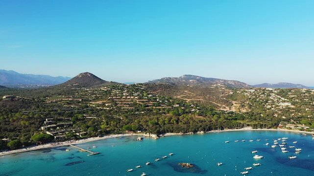Scenic aerial view of Plage de Santa Giulia with turquoise waters, boats, and lush hills in Corsica, France. Beautiful coastal landscape under a clear blue sky.