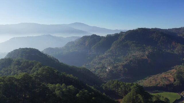 Scenic view of lush green mountains and misty valleys near Bontoc and Sagada in the Philippines, captured under clear blue skies.