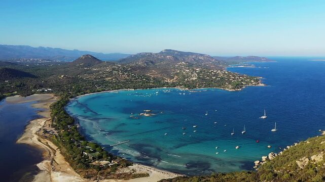 Scenic aerial panorama of Santa Giulia Beach with turquoise waters, anchored boats, and lush coastal landscape in Corsica, France.
