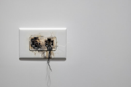 Prise &eacute;lectrique murale br&ucirc;l&eacute;e avec trace noire, fissure et fond gris avec espace n&eacute;gatif copyspace, visuel de panne &eacute;lectrique, court-circuit, s&eacute;curit&eacute; domestique, &eacute;lectricit&eacute; et assurance habitation