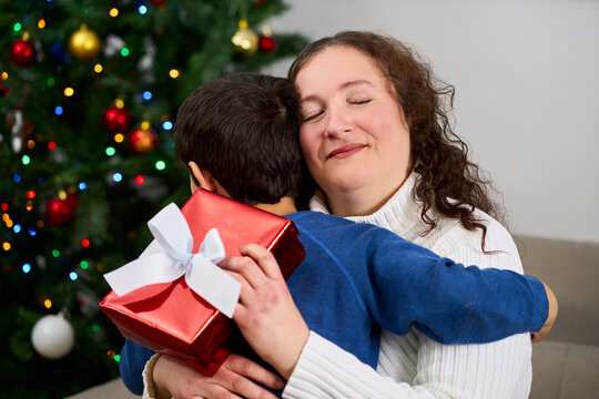 Christmas, gift and hug with mother, son and bonding together with decoration, house and festive in lounge. Xmas tree, family and parent with boy, embrace and present with happiness, holiday and love
