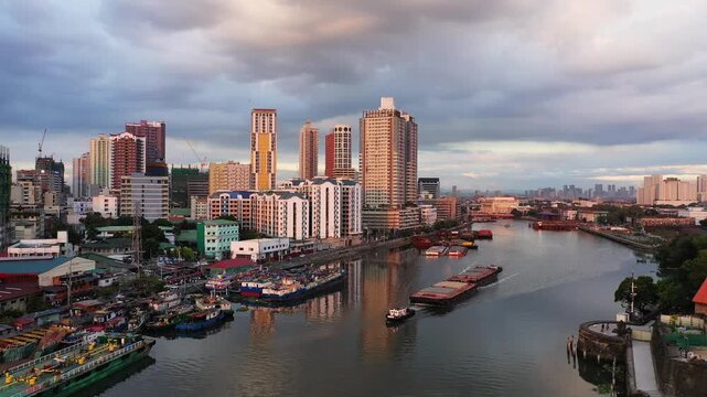 Cityscape of Manila with boats navigating the Pasig River under dramatic evening clouds, surrounded by modern high rise buildings.