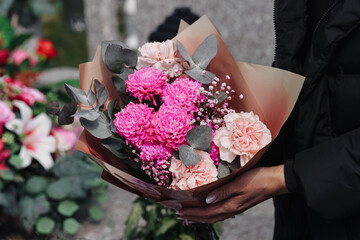 Bouquet of pink flowers held at cemetery during memorial visit. Floral arrangement symbolizing...