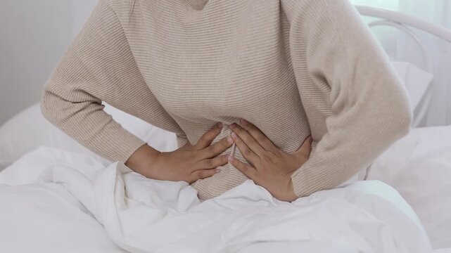 woman suffering stomach pain sitting on bed, abdominal cramps and discomfort, illness, healthcare concept, digestive problem.