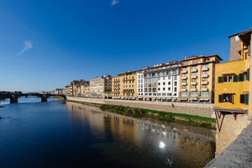 Fototapeta premium Historic Buildings Along Arno River in Florence, Italy with Bridge and Clear Blue Sky
