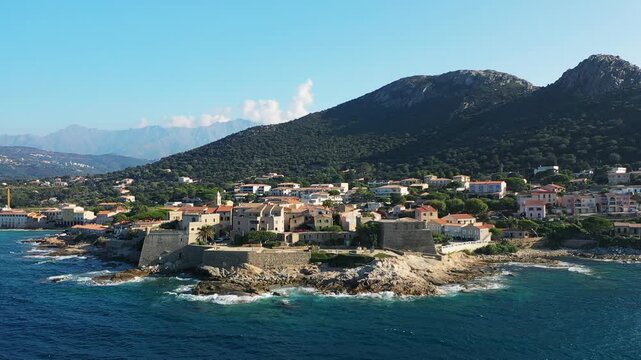 Aerial view of the historic coastal fortress and picturesque town of Calvi on the Mediterranean island of Corsica, surrounded by mountains and deep blue sea.