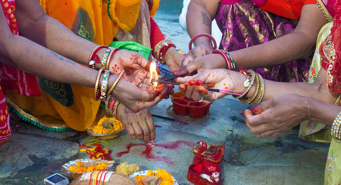 Close-up of four Women crouching on the ground lighting a traditional oil lamp (Diya), India