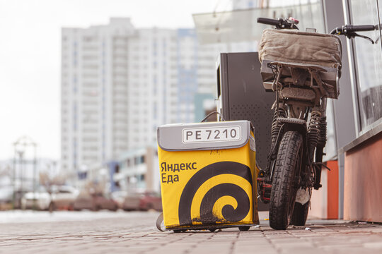 Krasnoyarsk, Russia 19 03 2026: Yandex Eda courier bike and delivery box on urban street, Russian food delivery service in real environment, last mile logistics concept