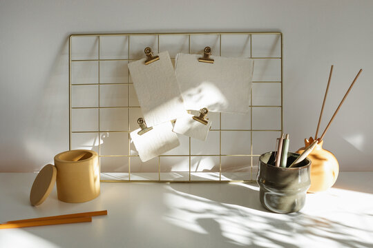 Blank pieces of card attached to a metal grid mood board with crocodile clips on a desk with assorted stationery