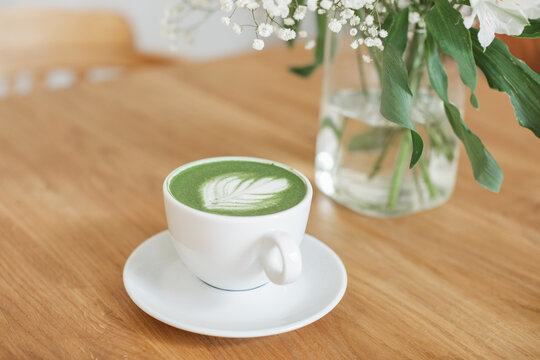 Close-up of a matcha latte hot drink on a wooden table next to a bouquet of flowers in a vase