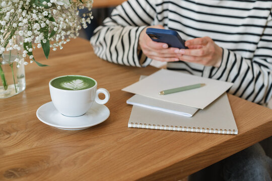 Close-up of a woman sitting in a cafe using a mobile phone and drinking a matcha latte