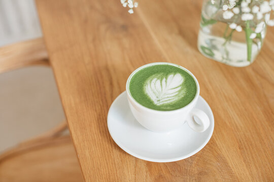 Close-up overhead view of a matcha latte hot drink on a wooden table next to a bouquet of flowers in a vase