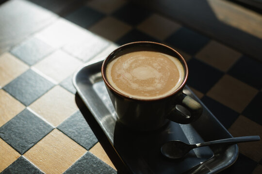 Close-up of a cup of black coffee on a metal tray on a checked table