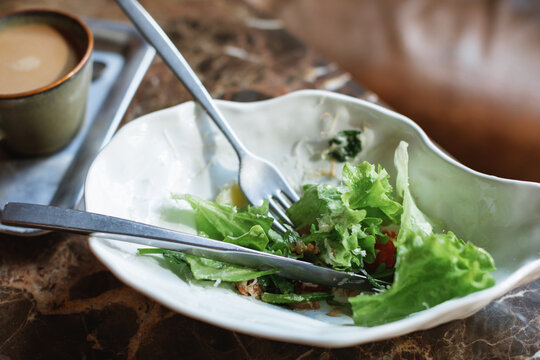 Close-up of a partially eaten green salad with smoked stracciatella cheese and a coffee on a table