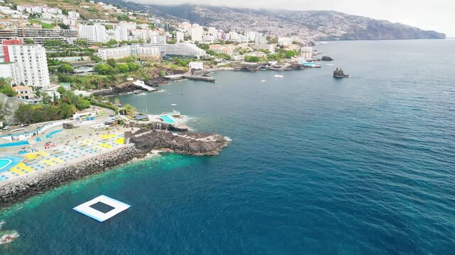 Dramatic aerial drone view of Ponta Gorda in Madeira, capturing rugged cliffs, coastal waters, and scattered urban buildings from above