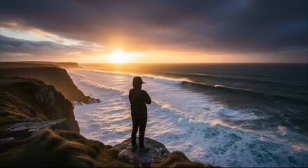 Fototapeta premium Person Standing on High Cliff Overlooking Stormy Ocean at Sunset